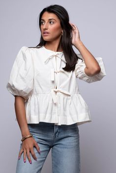 Effortlessly elevate your everyday look with our Norah Blouse. Featuring a timeless ivory color, delicate puff sleeves, and front ribbon ties, this peplum top exudes feminine charm. Hand Wash 100% Cotton Import Fit Guide Libby is 5ft 9 inches; Bust 34”, Waist 25”, Hips 34” Model is wearing a small True to size * Available at our Envy Location Luxury Puff Sleeve Shirt, Luxury Cotton Blouse For Party, Luxury Cotton Party Blouse, Luxury Cotton Feminine Blouse, Luxury Fitted Peplum Blouse, Luxury Fitted Puff Sleeve Top, Luxury Fitted Peplum Tops, Luxury Party Tops With Bow, Luxury Feminine Blouse For Party