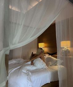 a woman sitting on top of a bed in a room with white sheets and curtains