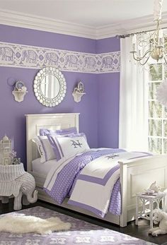 a purple and white bedroom with chandelier, bedding, rugs and pillows