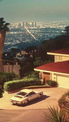 a car parked in front of a house on the side of a road with a city view behind it