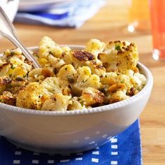 a white bowl filled with cauliflower on top of a blue table cloth next to a fork