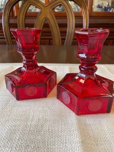 two red glass candlesticks sitting on top of a white tablecloth covered table