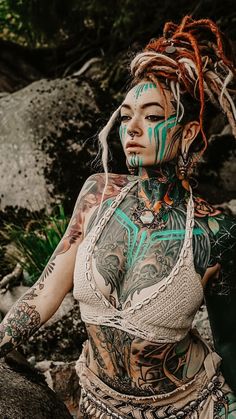 a woman with tattoos on her body standing next to rocks