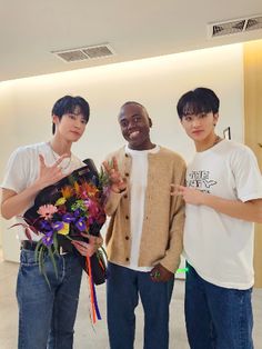 three young men standing next to each other in front of a wall with flowers on it