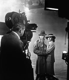 black and white photograph of two men standing in front of a camera with their arms crossed