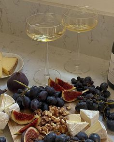 wine, cheese and grapes are on the counter next to two glasses of white wine