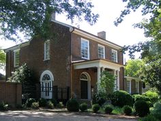 a large brick house with white trim on the front door and windows, surrounded by greenery