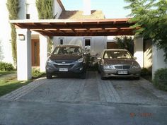 two cars parked in front of a house with a pergolan over the driveway