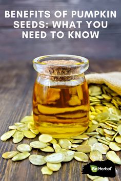 a glass jar filled with pumpkin oil sitting on top of a wooden table next to pumpkin seeds