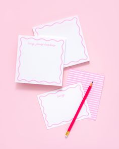 two notepads with writing on them next to a red pencil and pink background