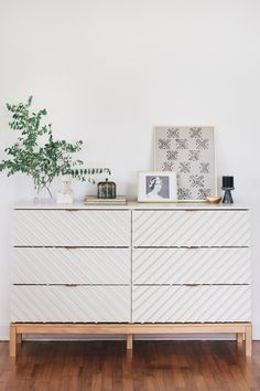 a white dresser sitting on top of a wooden floor next to a potted plant