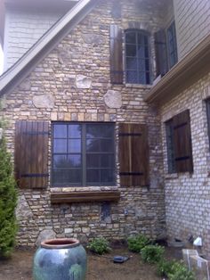 a large vase sitting in front of a brick building with shutters on the windows