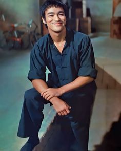 a young man sitting on top of a cement step smiling at the camera with his arms crossed