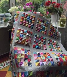 a quilted chair sitting in front of a window with potted flowers on it