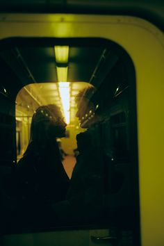 two people are sitting on a train looking at each other through the window and kissing