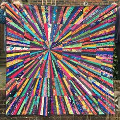 a person holding up a large colorful quilt