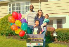 a family posing for a photo in front of a house with balloons on the lawn