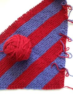 a red and blue striped knitted placemat with yarn