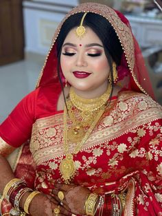 a woman in a red and gold bridal outfit with her hands on her chest