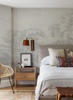 a bedroom with a bed, nightstand and chair in front of a wallpapered tree