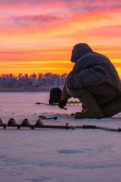 a man squatting down on the snow with skis and poles in front of him