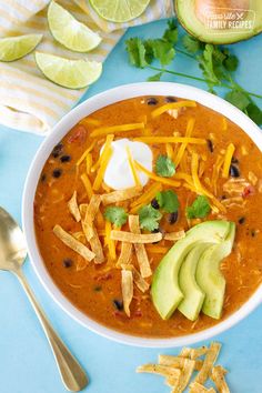 a bowl of chili cheese soup with tortilla chips and avocado on the side