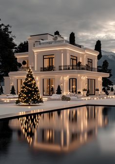 a christmas tree is lit up in front of a large white house with a pool