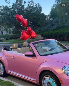 a pink convertible car with heart shaped balloons in the back seat, parked next to a curb