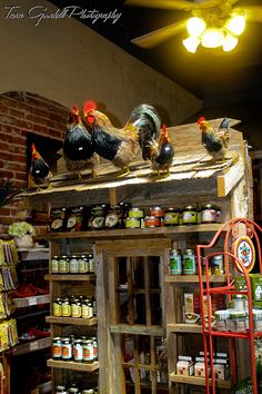 roosters are perched on top of the roof of a store's display case