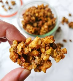 a person holding up some food in front of a small glass bowl filled with nuts