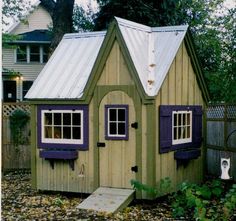 a small wooden house with purple shutters on the windows and a white roof sits in front of a fence