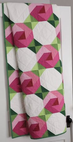 a pink and green quilt hanging on the wall