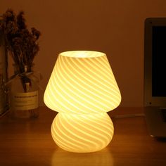 a white lamp sitting on top of a wooden table next to a laptop and flowers