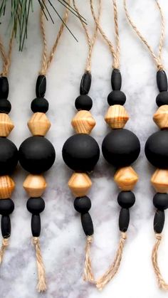 black and wood bead necklaces hanging from rope on marble surface with pine tree branch in background