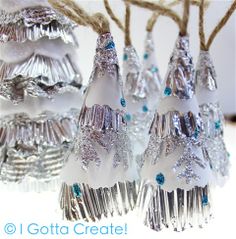 three silver and white christmas trees are hanging from twine with blue crystals on them