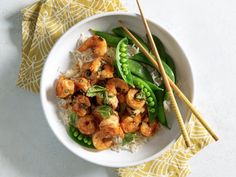 a white bowl filled with shrimp and rice next to chopsticks on top of a yellow napkin