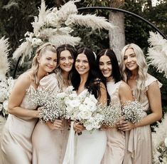 a group of women standing next to each other in front of a white flower arch