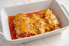 two enchiladas in a white casserole dish on a marble counter