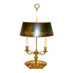 a brass table lamp with two candles on the bottom and a black shade over it