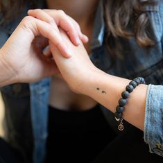 a woman wearing a blue jean jacket holding her wrist with a small tattoo on it