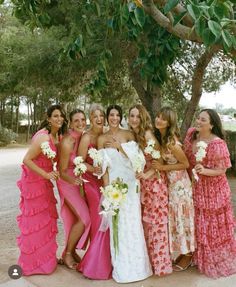 a group of women standing next to each other under a tree with flowers in their dresses