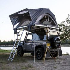 an off - road vehicle parked next to a lake with a tent on the roof