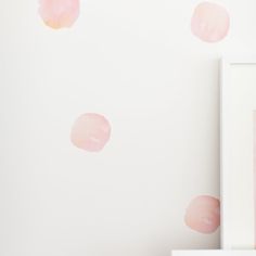 pink watercolor spots are on the wall next to a white frame and vase with flowers in it