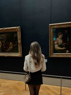 a woman standing in front of two paintings looking at each other with her back to the camera