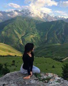 a woman sitting on top of a large rock in the middle of a mountain range