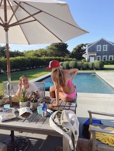 two women sitting at a table with an umbrella over their head, near a pool