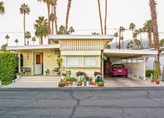 a red car parked in front of a yellow house with palm trees on both sides