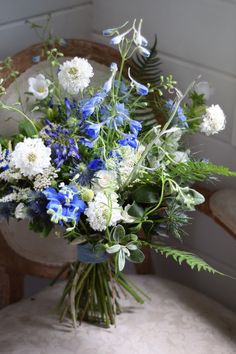 a vase filled with blue and white flowers sitting on top of a wooden chair next to a wall