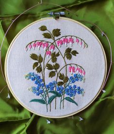 a close up of a embroidery on a green cloth with pink, blue and white flowers