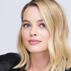 a woman with blonde hair and blue eyes looks at the camera while wearing a black jacket